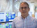 Portrait of Kevin Cern standing in front of computer monitors.