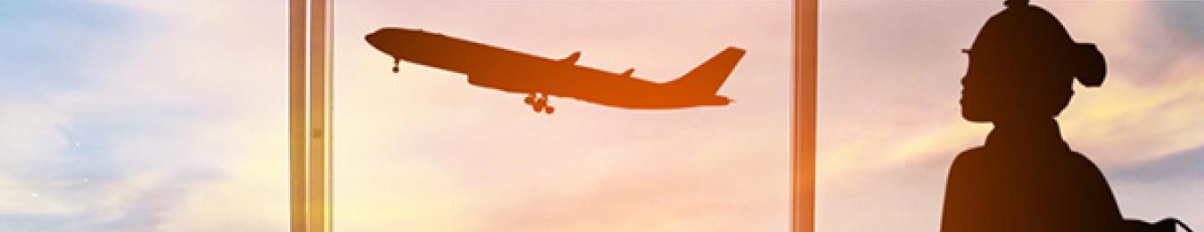 Woman in airport looks out the window at a plane taking off.