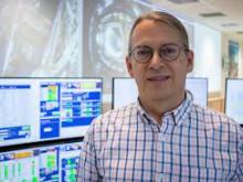 Portrait of Kevin Cern standing in front of computer monitors.